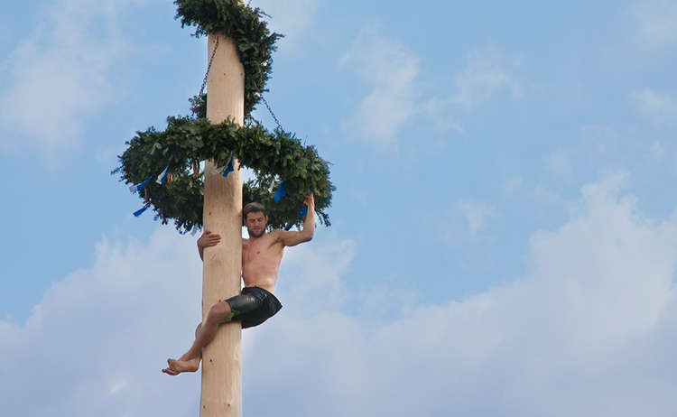 Ein kräftiger Bursch' kraxelt auf den Maibaum